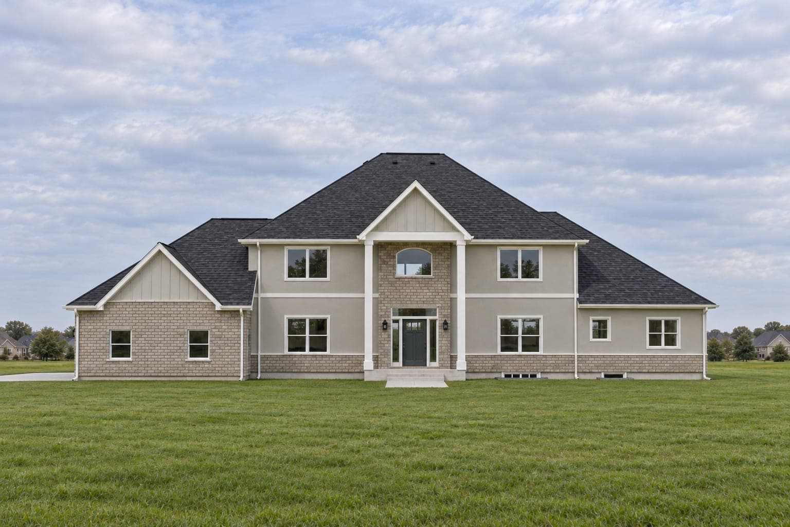 Front of a two-story transitional home in greige siding and stone with a two-story columned entry, an arched window and hip roofs
