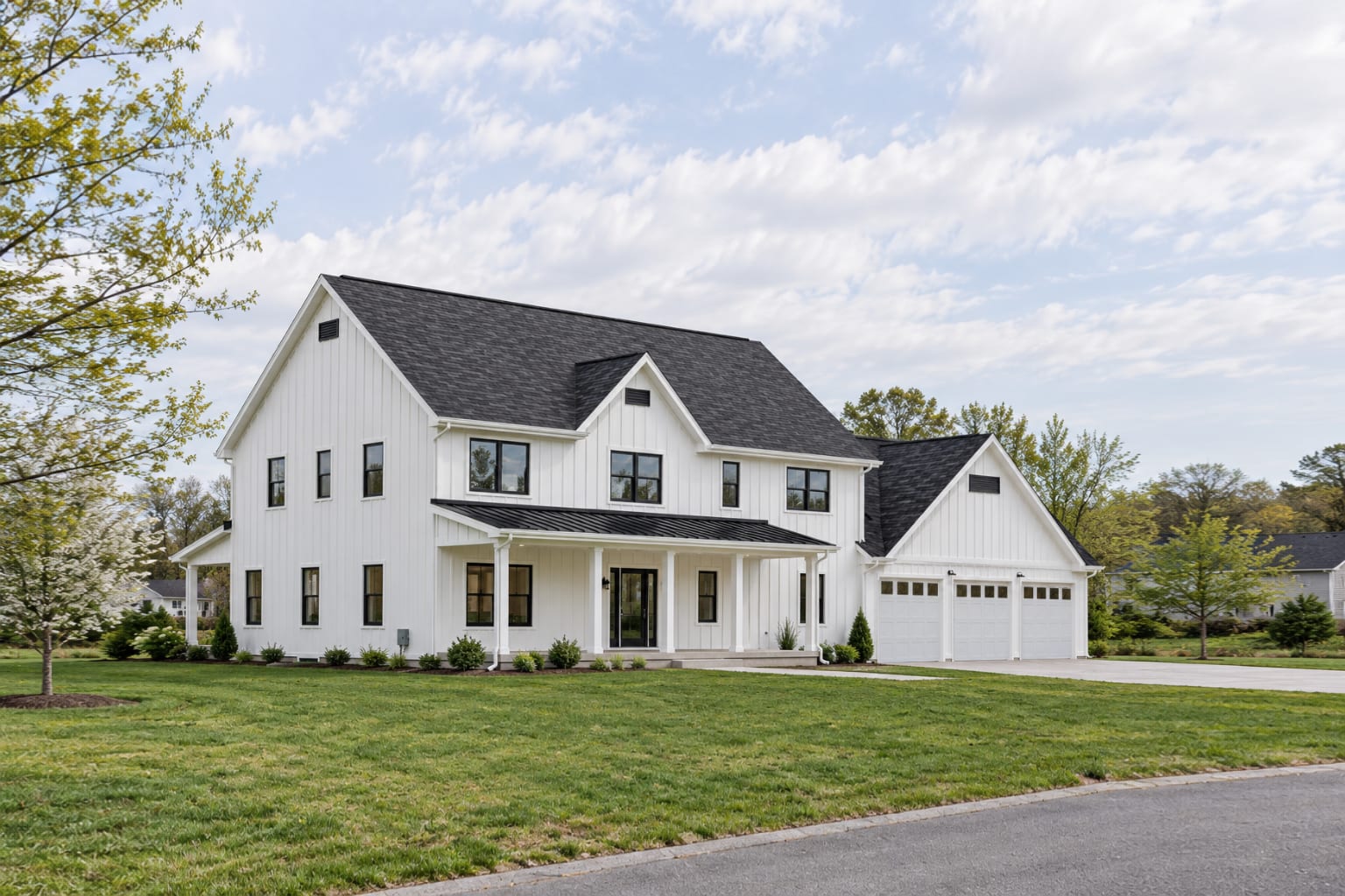 White two-story modern farmhouse from the front corner, showing the gables and long front porch