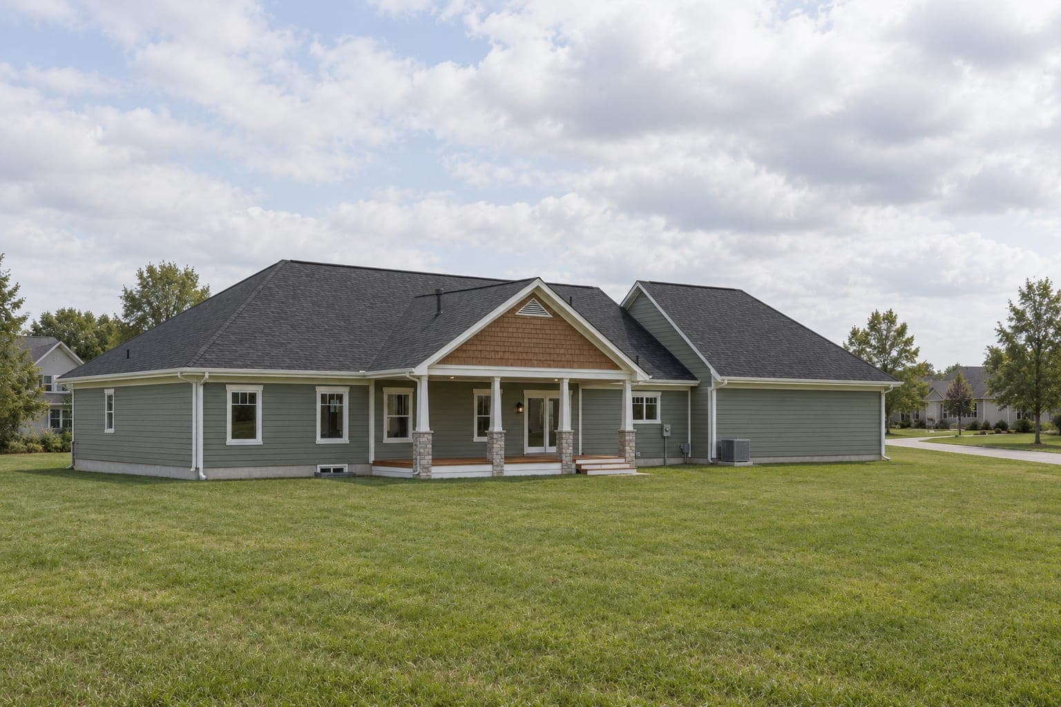 Back of the sage-green ranch with a covered rear porch on stone-based columns and a shake gable